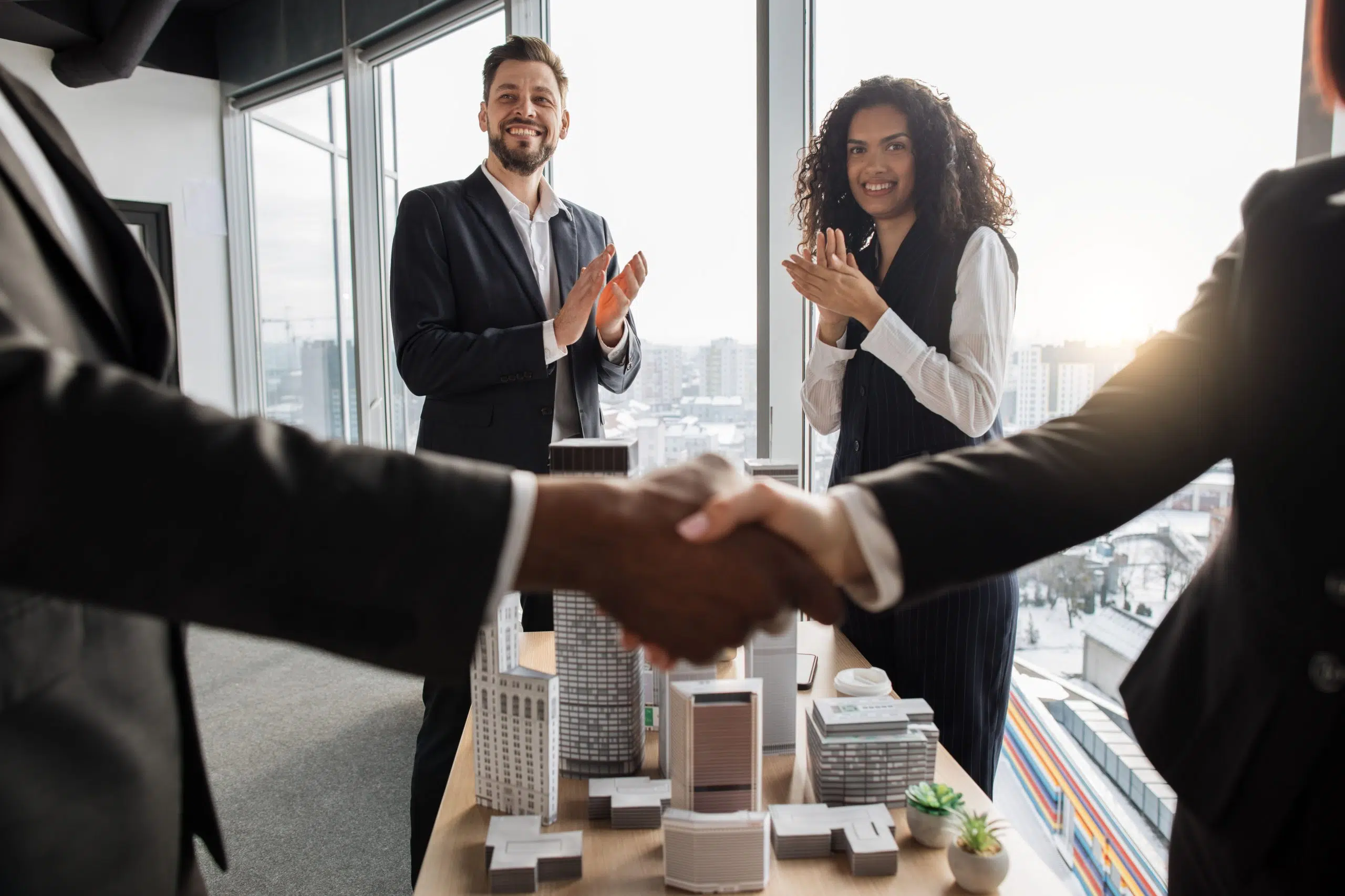 Selective focus on two business people applauding and their colleagues businesspeople real estate, agents developers handshake after successful deal, city district urban planning project good work.